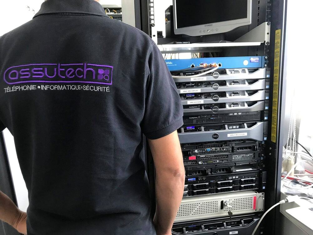 Technicien Assutech en polo devant une baie de serveurs, en intervention chez un client